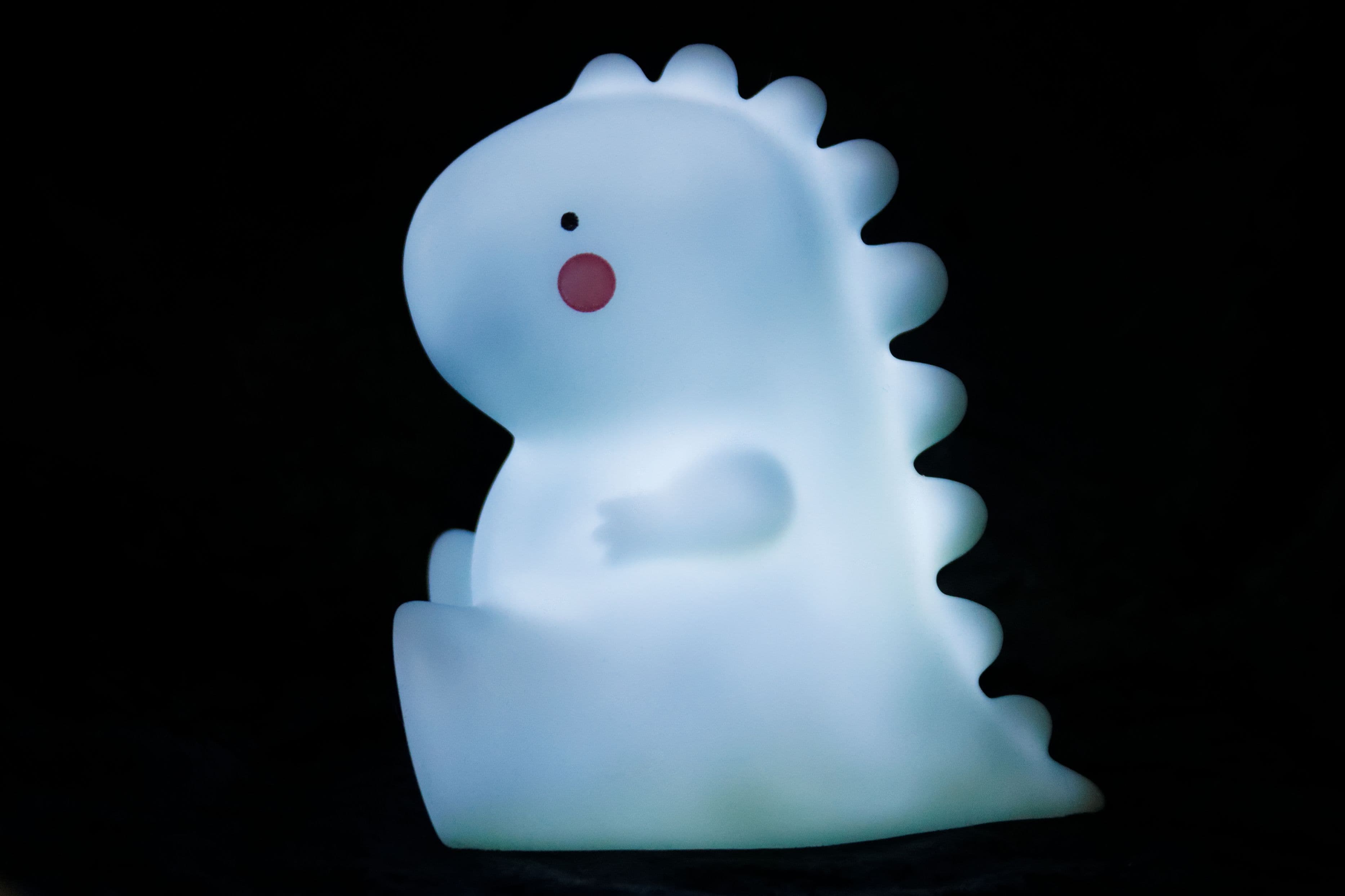 Small dinosaur-shaped night light glowing pale blue against a dark background