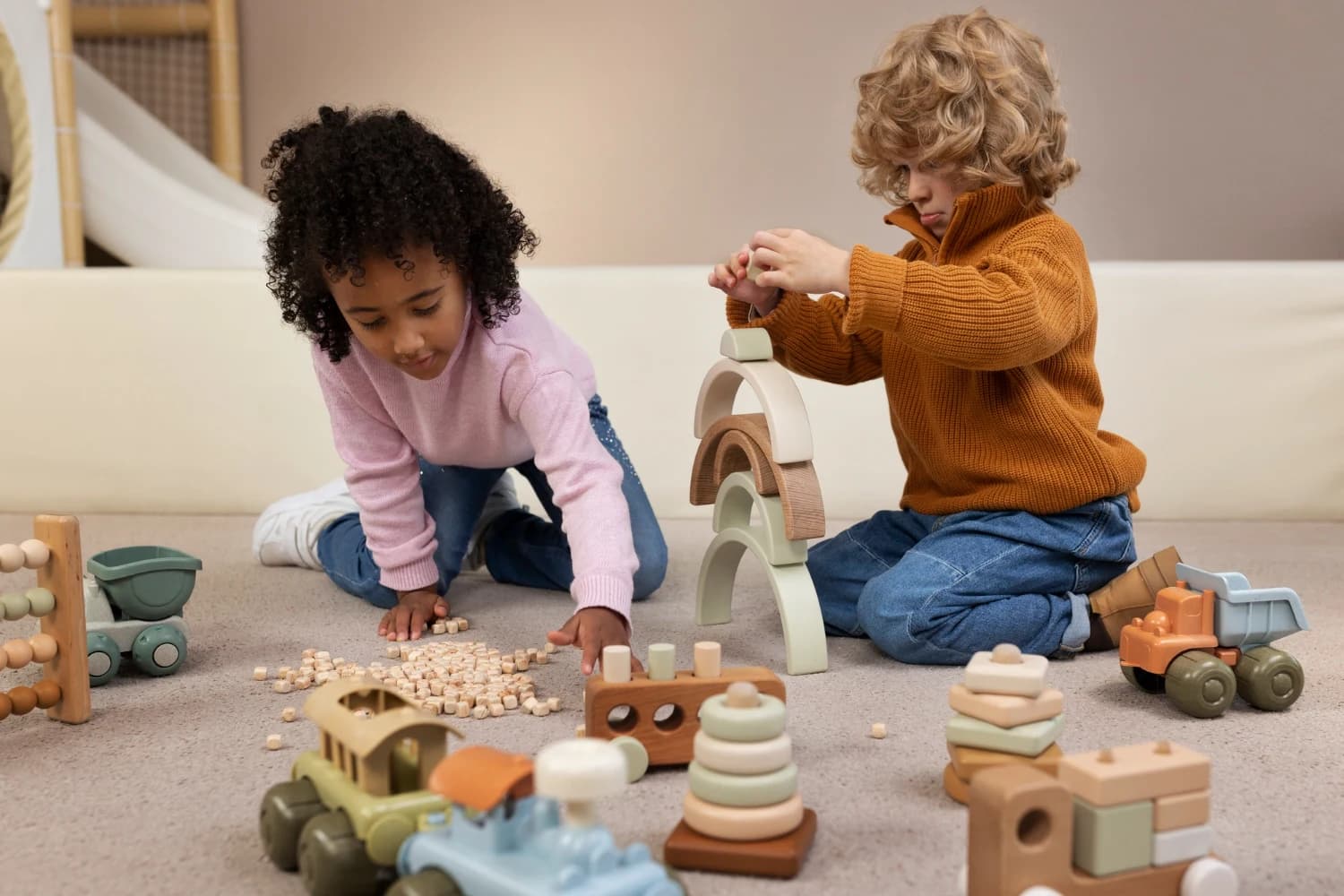 Two children playing on the floor with wooden toys, including a stacking rainbow and a wooden truck